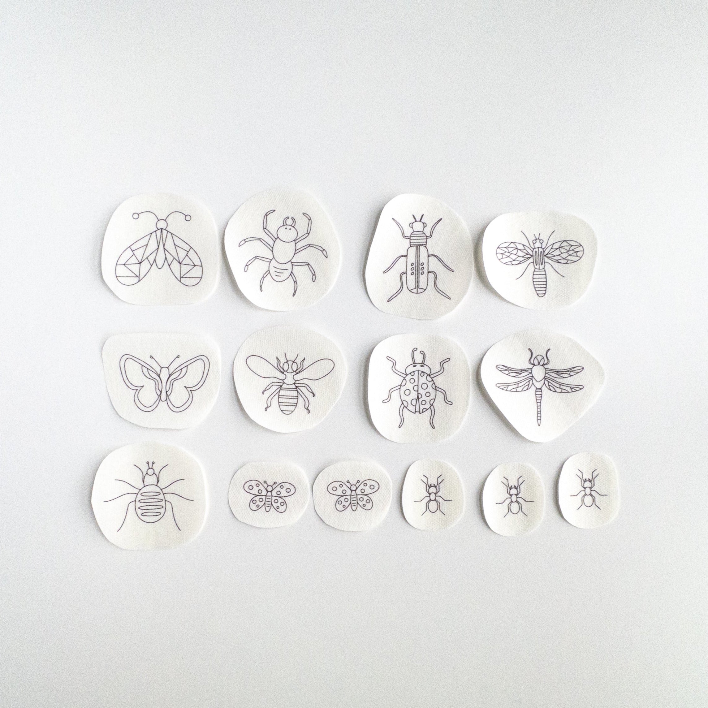 14 black outline insect embroidery patterns on white water-soluble stabilizer patches, assorted bug designs and sizes.