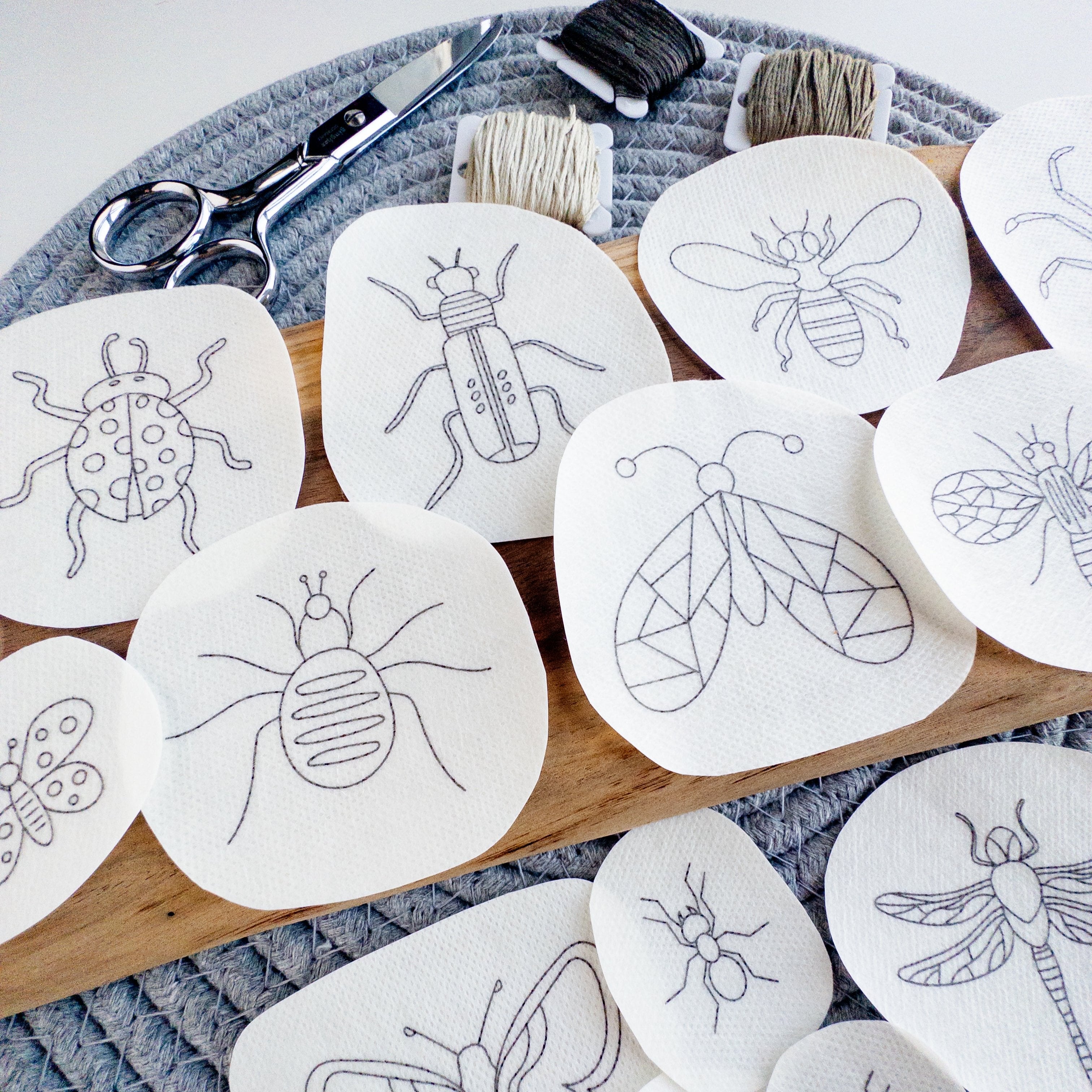 Assorted insect stick and stitch embroidery patterns on white water-soluble stabilizer, with scissors and floss.