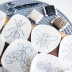 White water-soluble insect embroidery patterns: a beetle, bee, and butterfly, with thread and scissors.