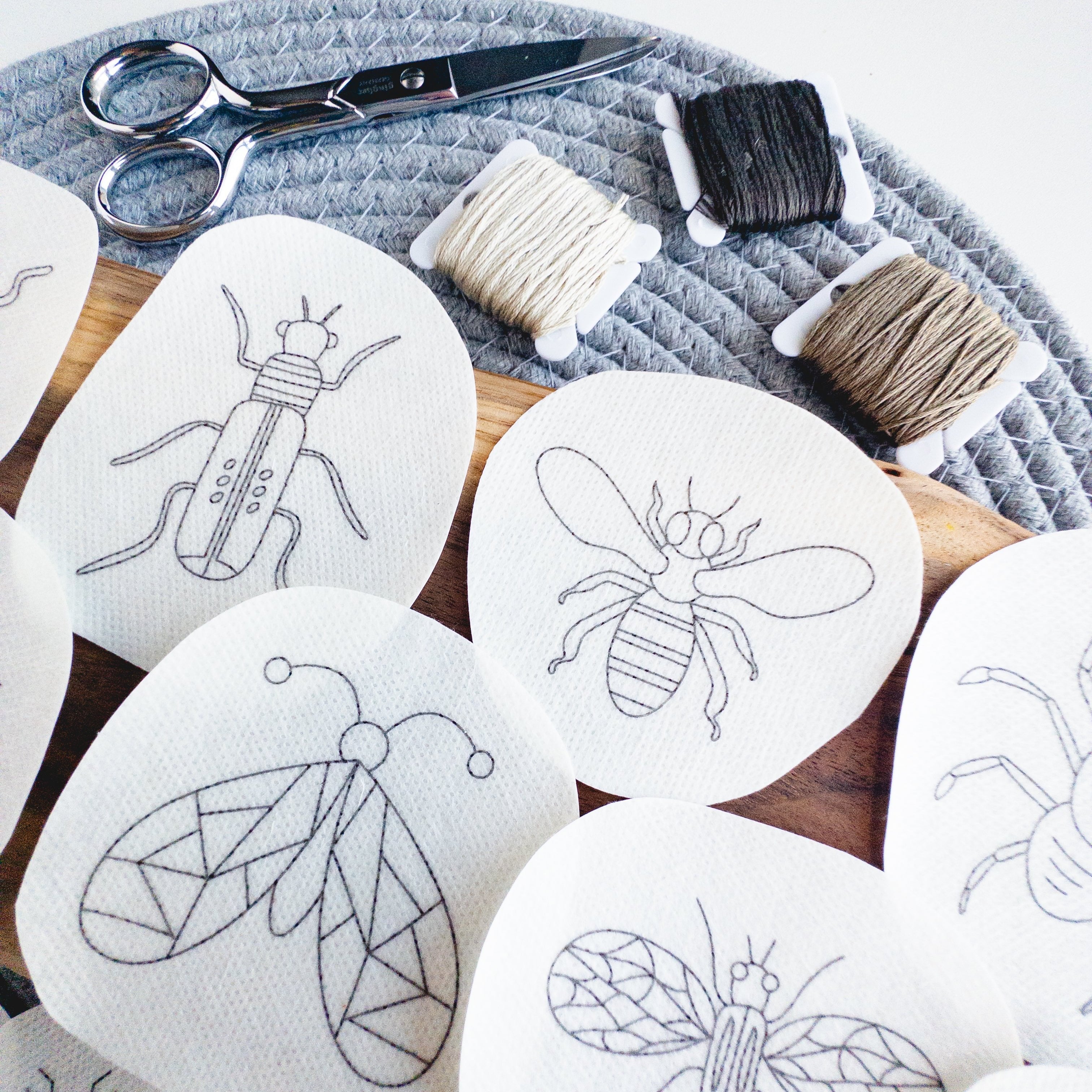 White water-soluble insect embroidery patterns: a beetle, bee, and butterfly, with thread and scissors.