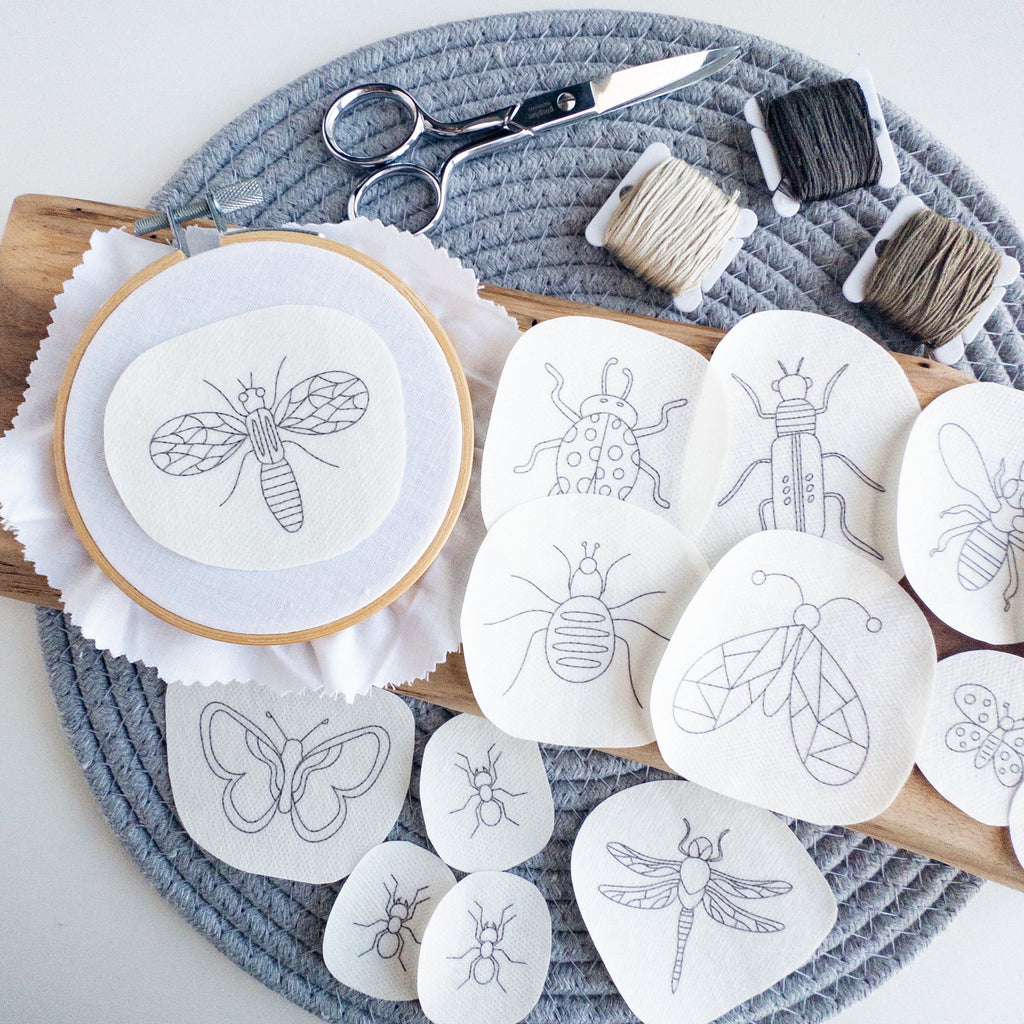 Assorted insect stick and stitch embroidery patterns on water-soluble stabilizer, with a hoop, scissors, and floss.