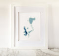 Framed Okoboji Iowa Lakes cross-stitch pattern in shades of blue on white fabric.