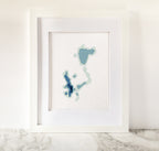 Framed Okoboji Iowa Lakes cross-stitch pattern in shades of blue on white fabric.