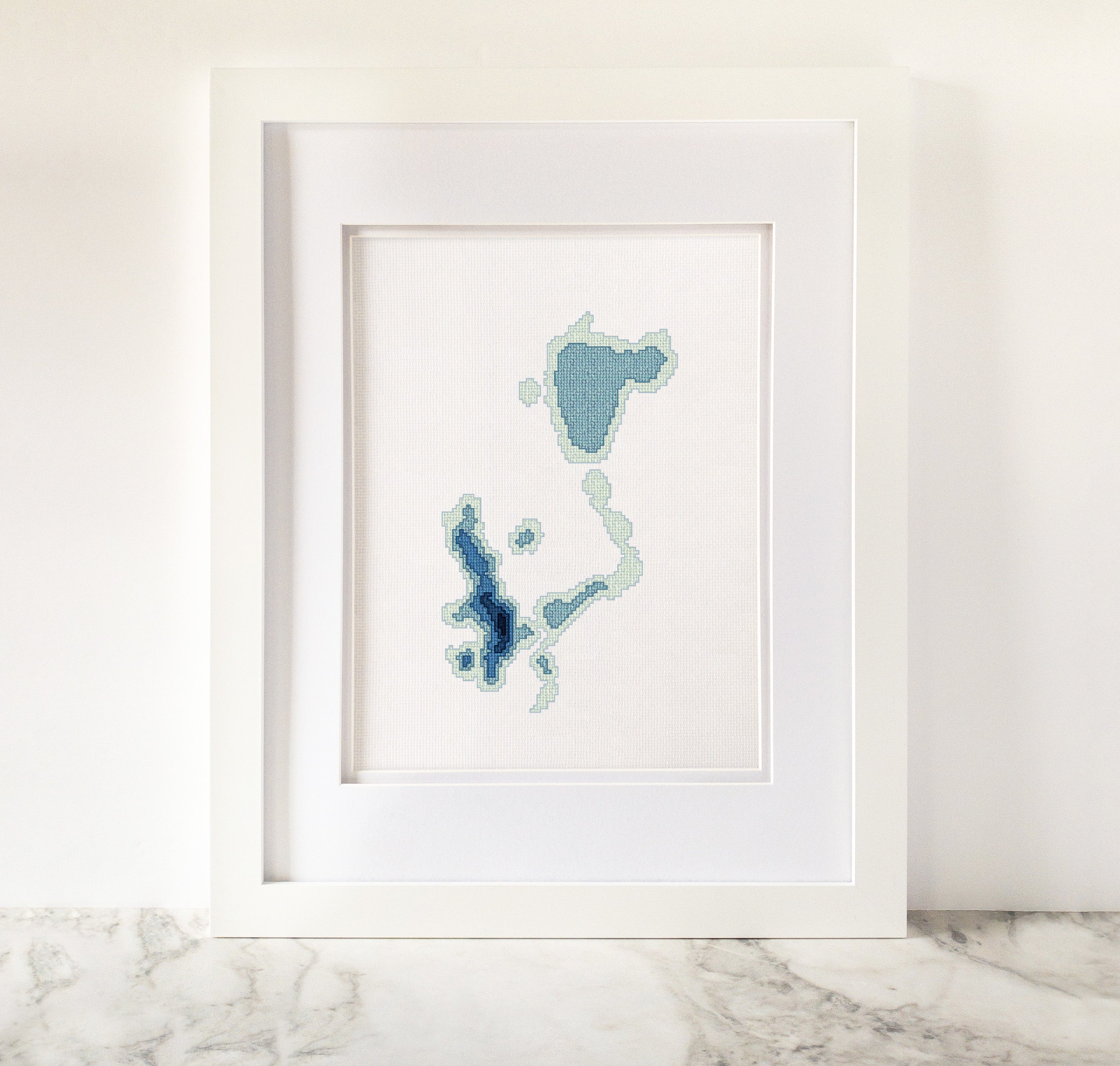 Framed Okoboji Iowa Lakes cross-stitch pattern in shades of blue on white fabric.