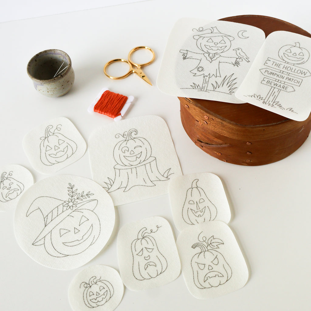 Washaway stabilizer sheets with ten black-outlined Jack O'Lantern embroidery patterns, scissors, and orange floss.