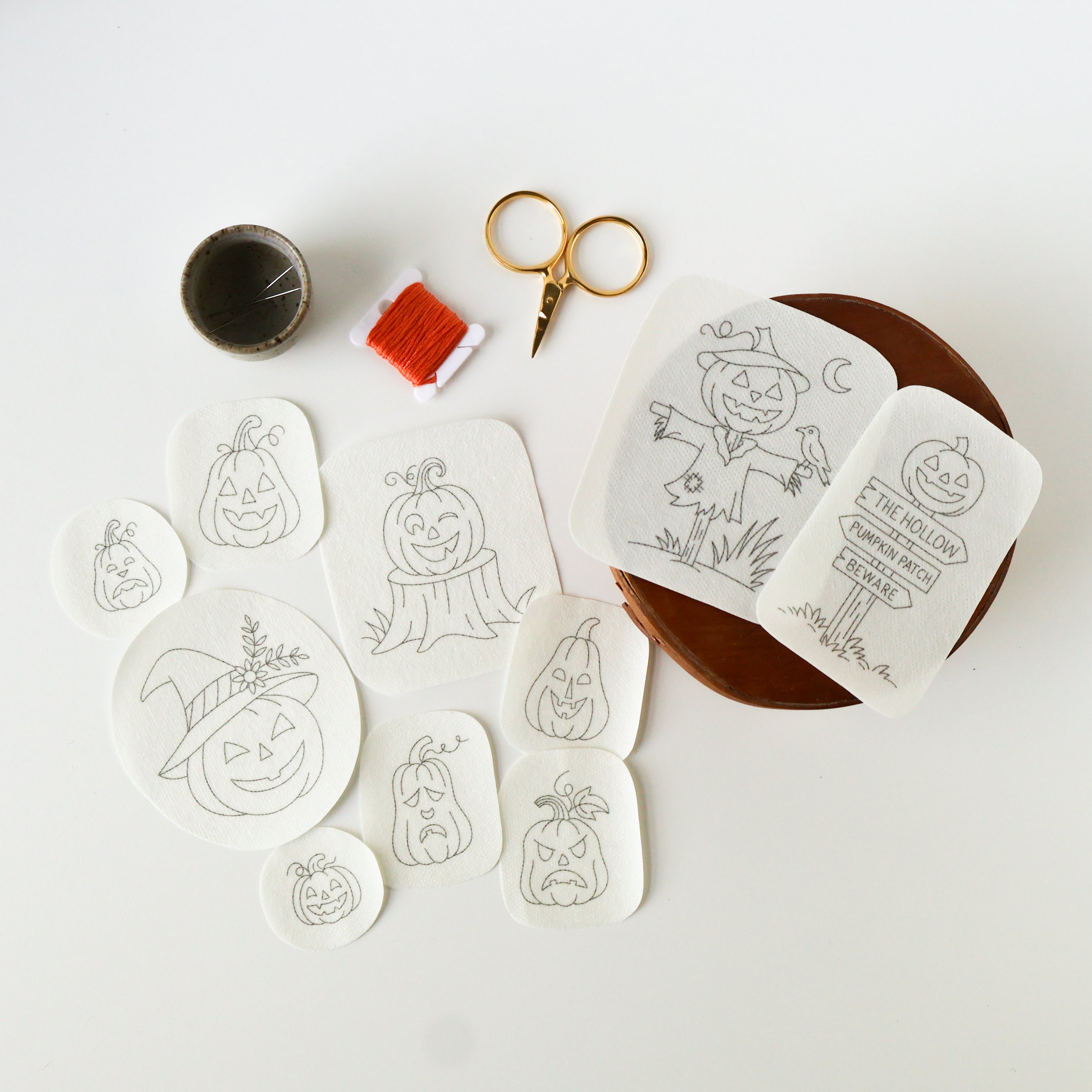 Ten white washaway embroidery patterns featuring various Jack O'Lanterns, a scarecrow, and a sign, with thread and scissors.