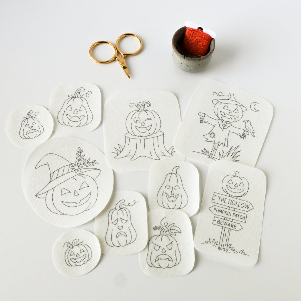 Ten Jack O'Lantern stick and stitch embroidery patterns on white washaway stabilizer, with gold scissors and orange floss.