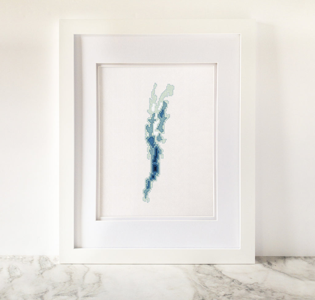 Framed Lake Champlain cross-stitch art, featuring a blue and green bathymetric map on white fabric.
