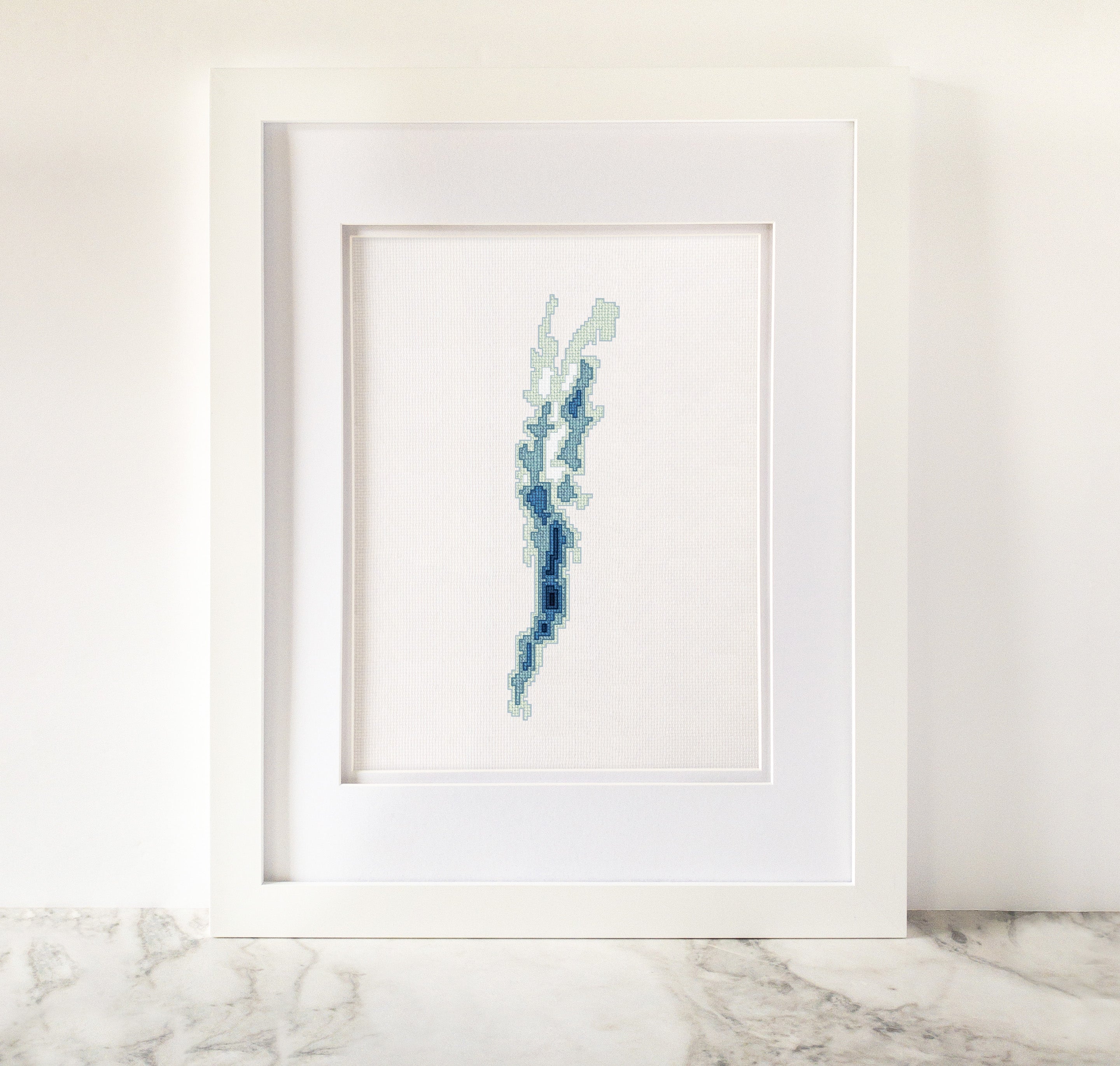 Framed Lake Champlain cross-stitch art, featuring a blue and green bathymetric map on white fabric.