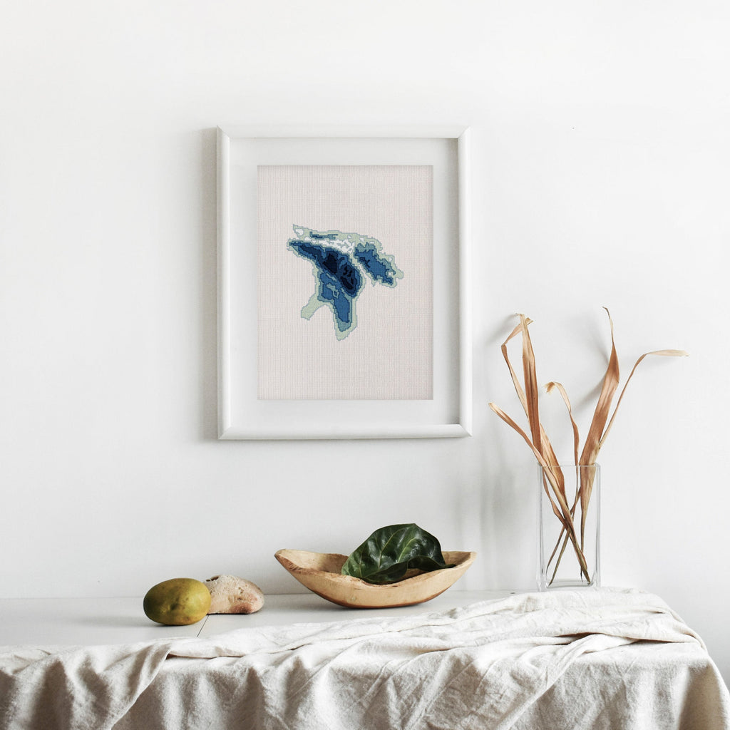 Framed Lake Huron cross-stitch pattern in blue and white, displayed on a minimalist white wall.