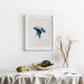 Framed Lake Huron cross-stitch pattern in blue and white, displayed on a minimalist white wall.