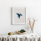 Framed Lake Huron cross-stitch pattern in blue and white, displayed on a minimalist white wall.