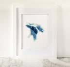 Framed Lake Huron cross-stitch art in shades of blue and green on white fabric.