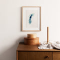 Framed Lake Michigan cross-stitch pattern in shades of blue, displayed above wooden boxes and a candle.