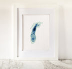 Framed Lake Michigan cross-stitch art with blue bathymetric map design on white fabric.