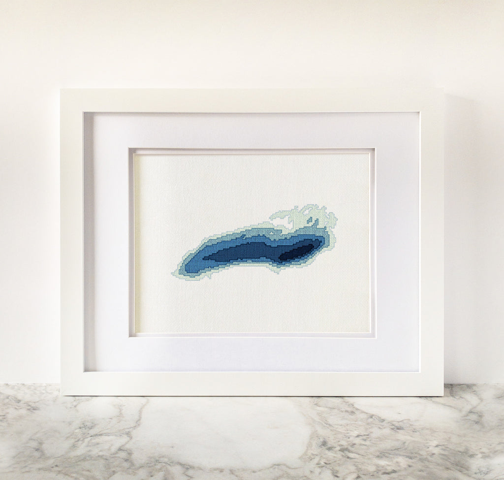 Framed Lake Ontario cross-stitch pattern with blue bathymetric map design on white fabric.