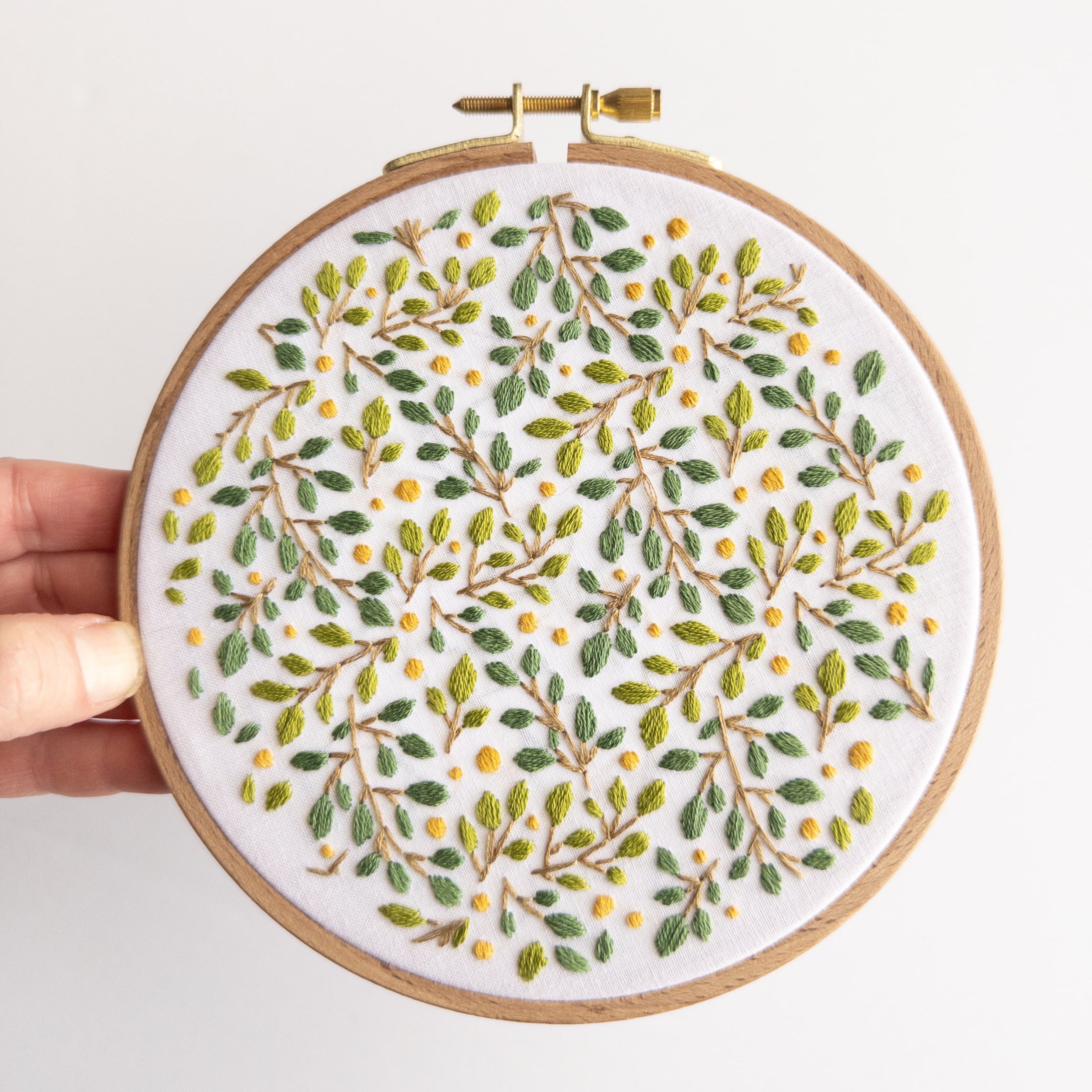 Embroidered lemon grove botanical design in a 6-inch wooden hoop, featuring green leaves and yellow berries.