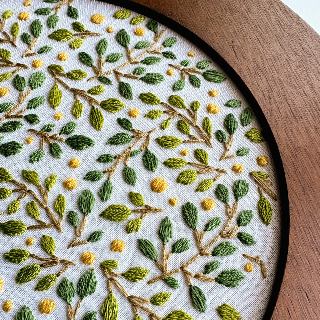 Embroidered abstract lemon grove design with green leaves and yellow dots in a wooden 6-inch hoop.