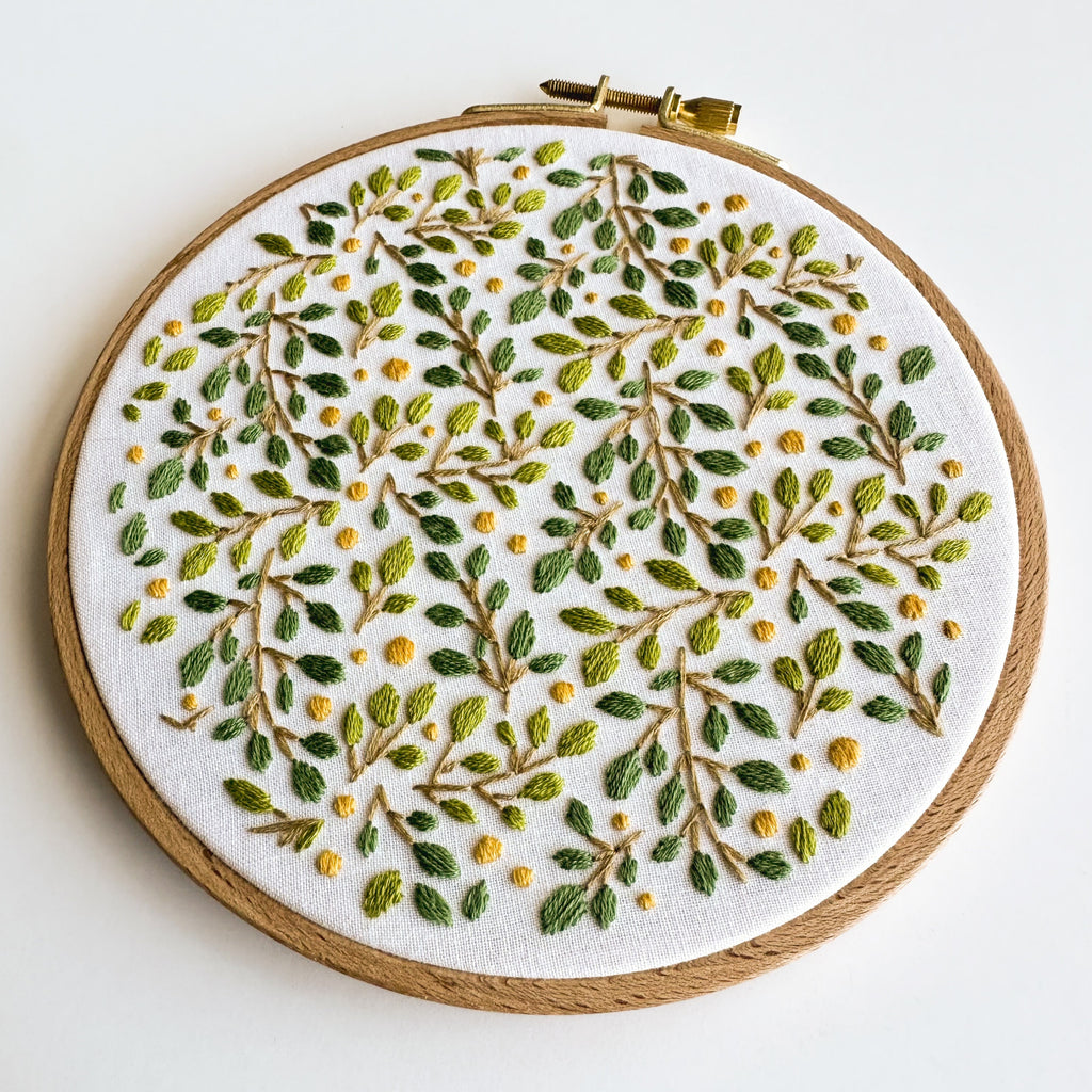 Embroidered lemon grove botanical design on white fabric in a 6-inch wooden hoop, featuring green leaves and yellow dots.