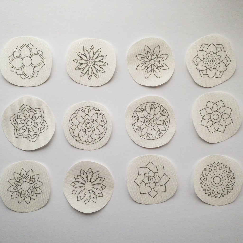 Twelve round, white water-soluble stick and stitch mandala embroidery patterns with gray outlines.