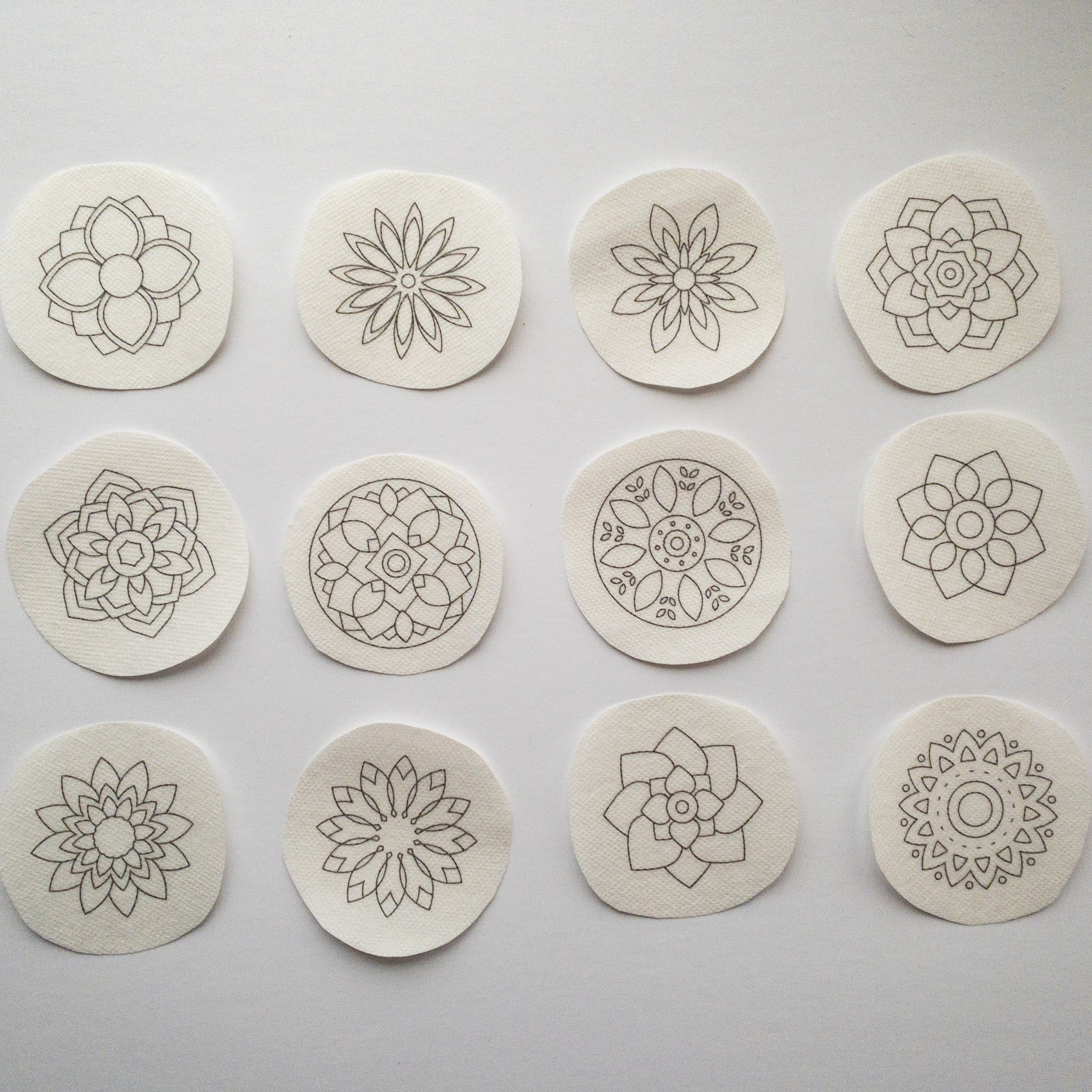 Twelve round, white water-soluble stick and stitch mandala embroidery patterns with gray outlines.