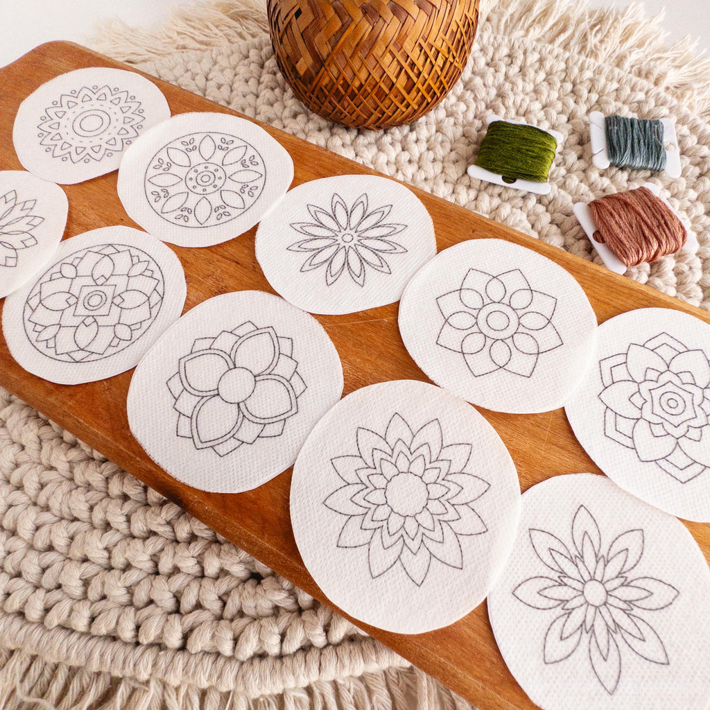 Twelve round, white mandala stick and stitch embroidery patterns on a wooden board with floss.