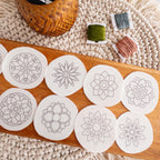 Ten round white stick and stitch mandala embroidery patterns on a wooden board with colorful floss.