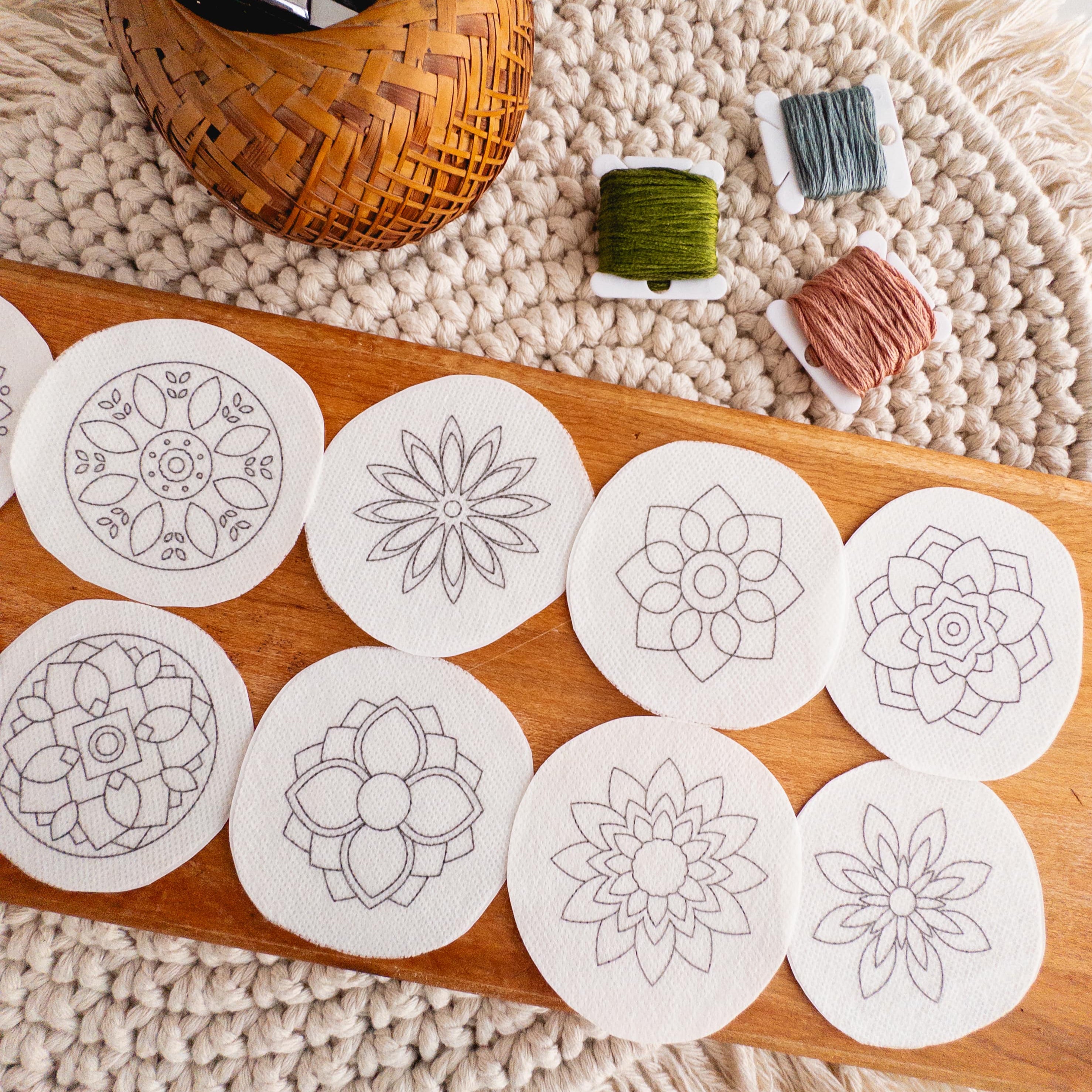 Ten round white stick and stitch mandala embroidery patterns on a wooden board with colorful floss.