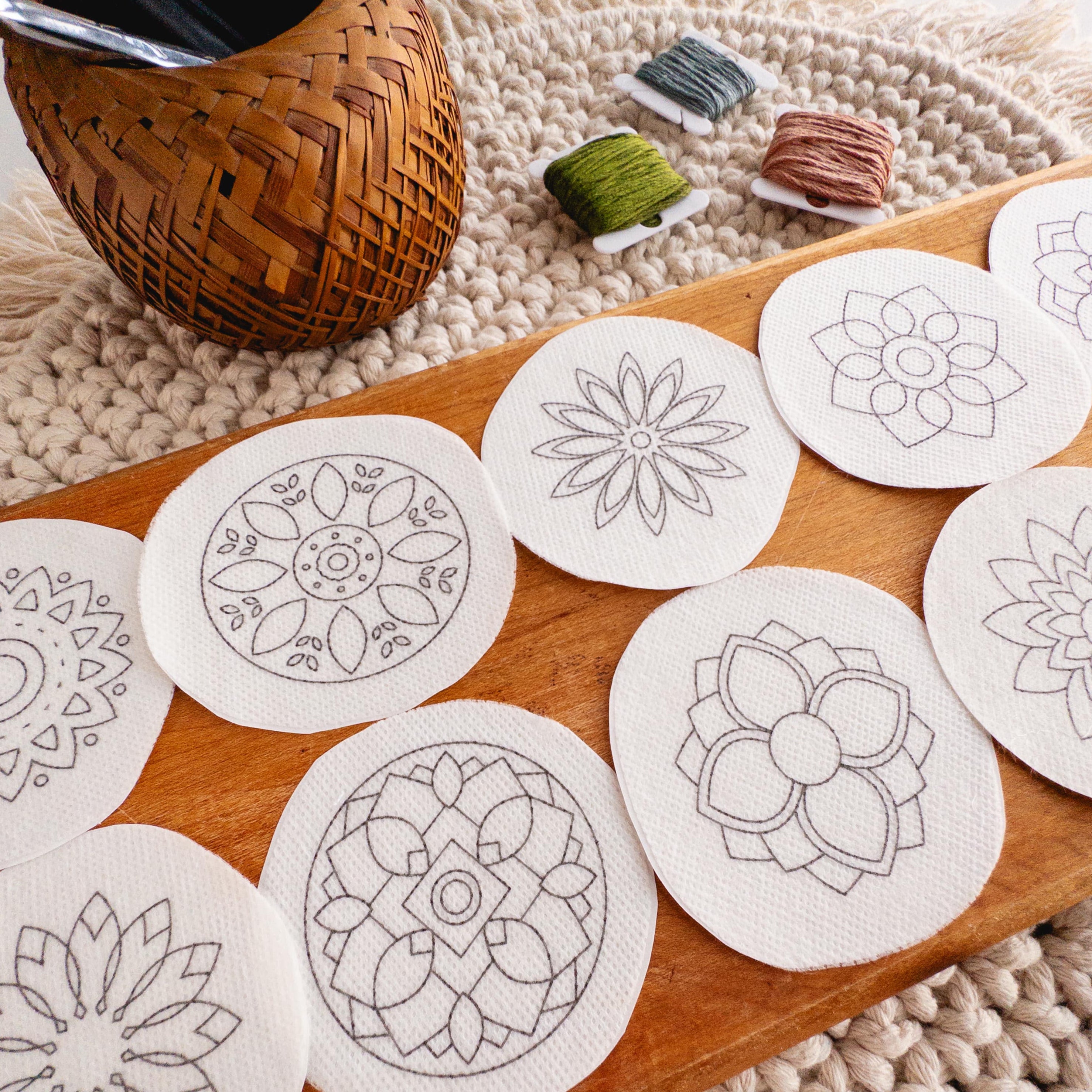 Circular white water-soluble mandala stick and stitch embroidery patterns on a wooden board with floss.