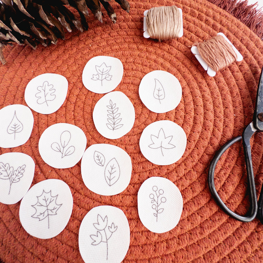 Mini autumn botanical stick and stitch embroidery patterns on white water-soluble stabilizer, with floss and scissors.