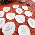 White water-soluble stick and stitch patches with various black outline autumn botanical designs on a rust-colored mat.