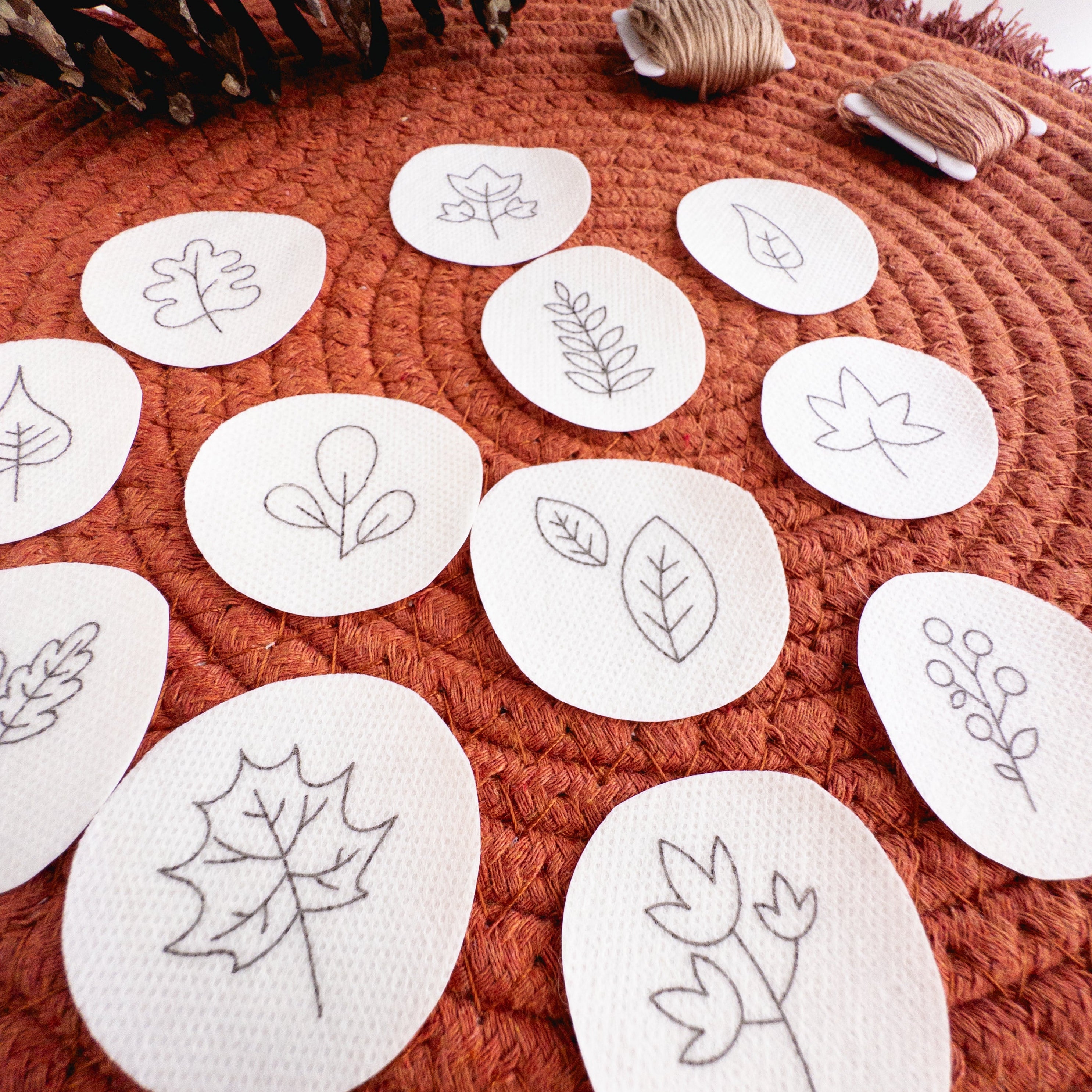 White water-soluble stick and stitch patches with various black outline autumn botanical designs on a rust-colored mat.