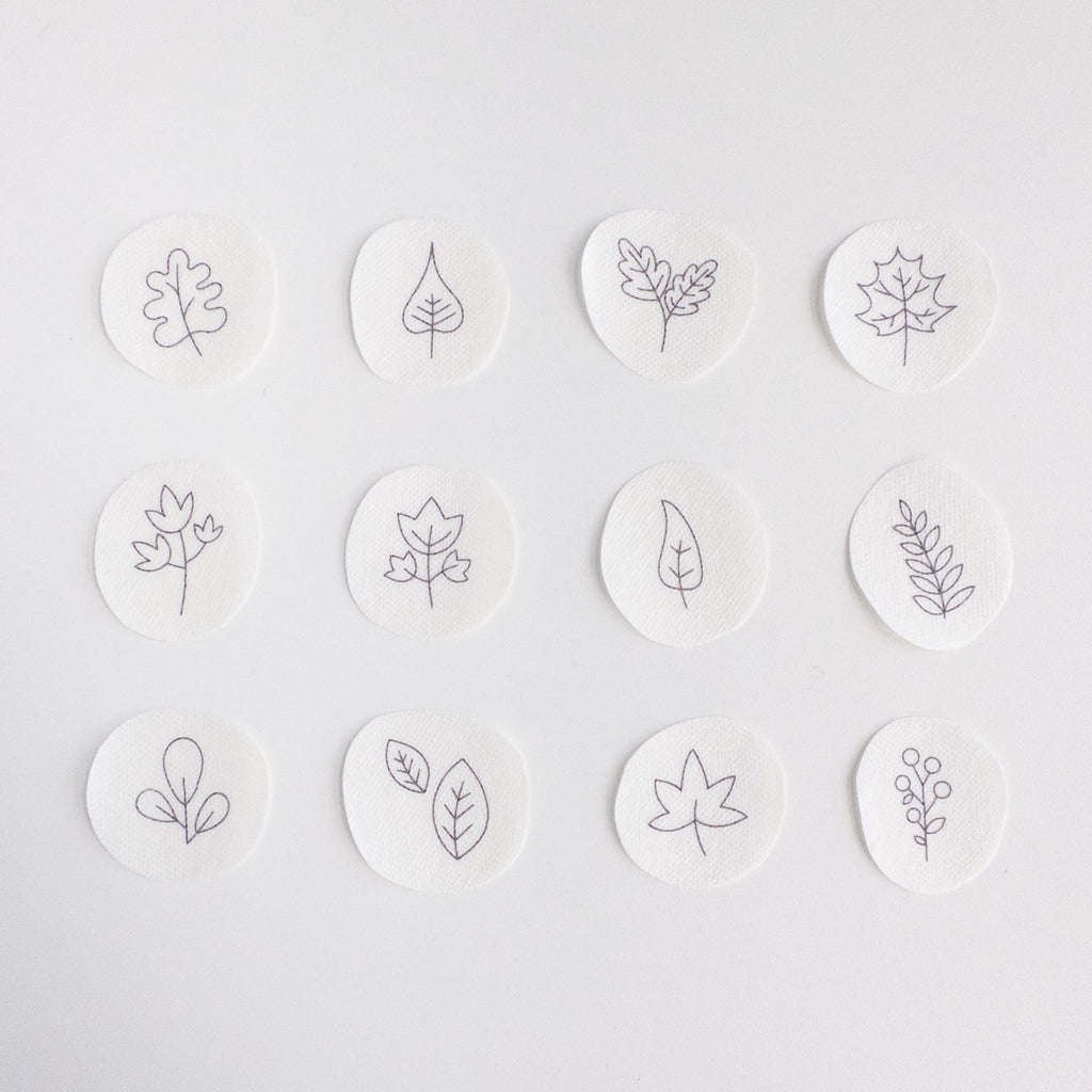 Twelve small, white, circular water-soluble patches with black outline autumn leaf and botanical embroidery patterns.