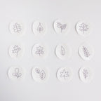 Twelve small, white, circular water-soluble patches with black outline autumn leaf and botanical embroidery patterns.