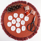 12 mini mushroom stick and stitch embroidery patterns on a terracotta mat with thread, pinecone, and scissors.