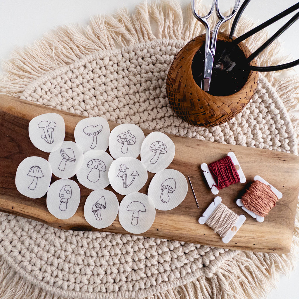Twelve mini mushroom stick and stitch embroidery patterns on water-soluble stabilizer, with floss and tools.