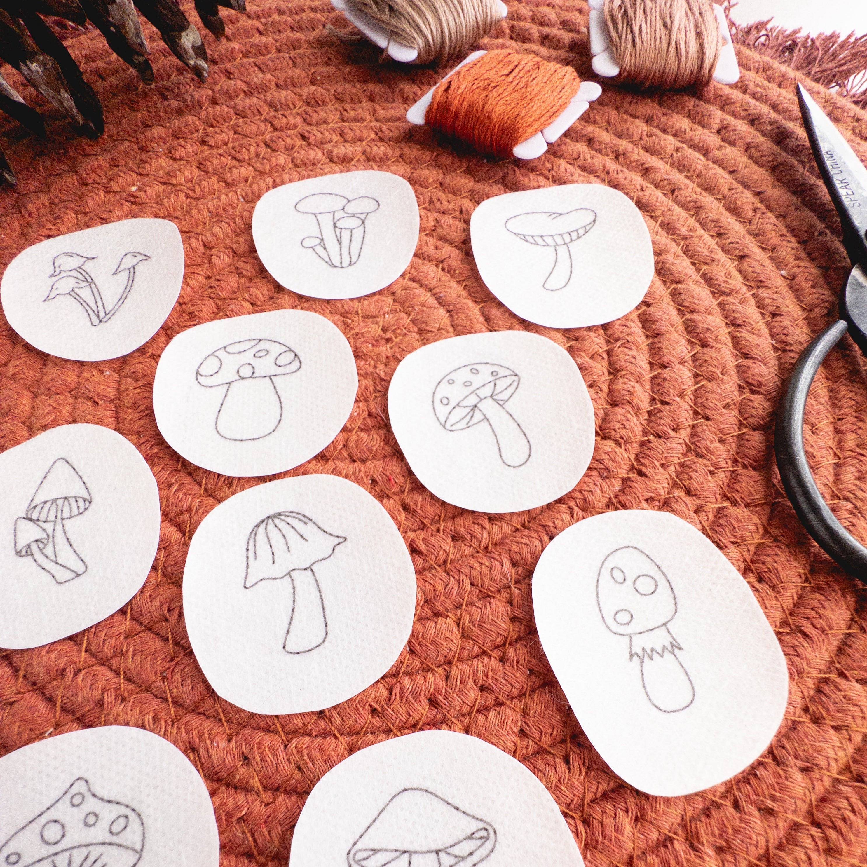 Twelve mini mushroom stick and stitch embroidery patterns on white water-soluble patches, with orange thread.