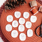 Twelve mini mushroom stick and stitch embroidery patterns on white water-soluble stabilizer, on a rust-colored mat.