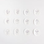 Twelve white, water-soluble stick and stitch patches featuring unique mini mushroom embroidery patterns.
