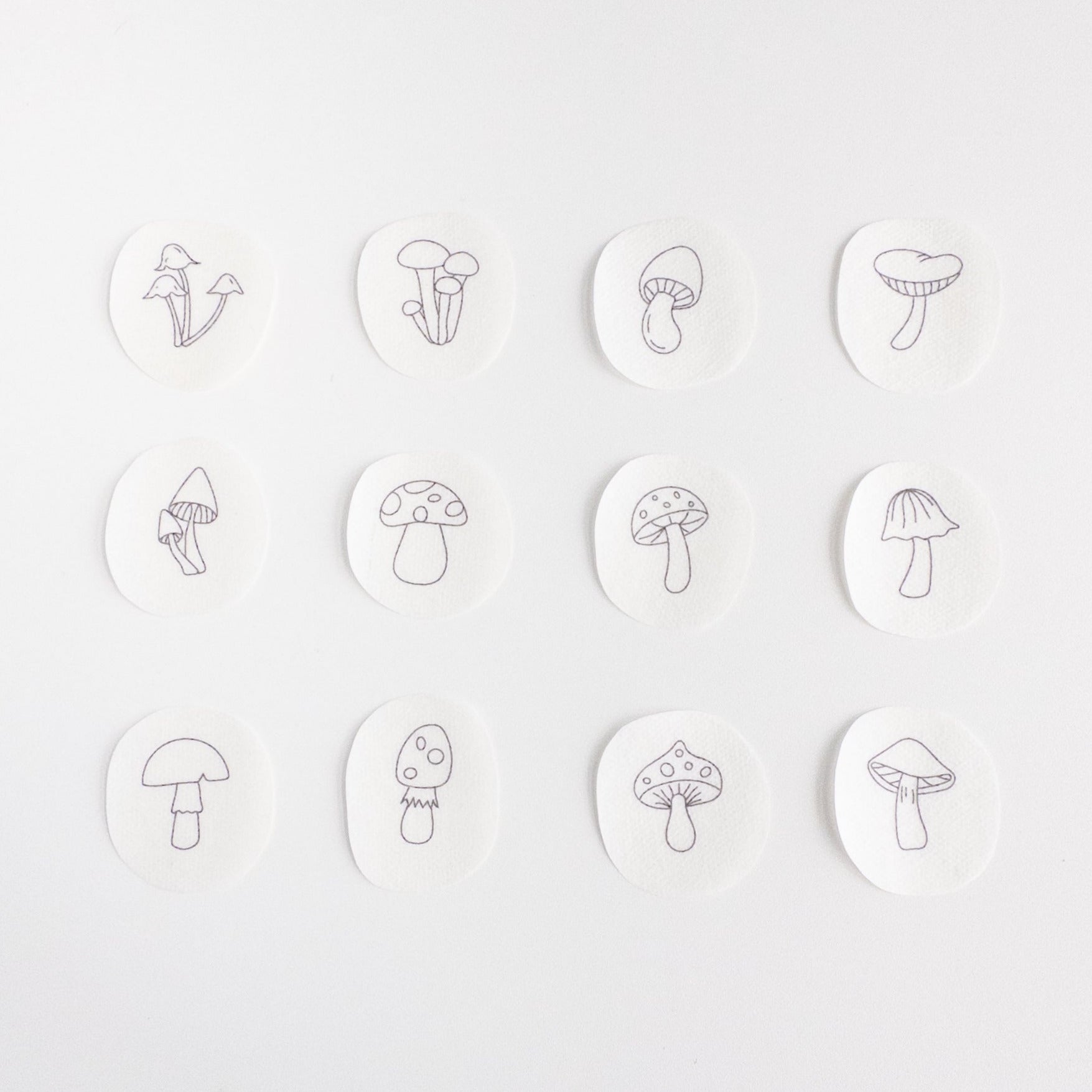 Twelve white, water-soluble stick and stitch patches featuring unique mini mushroom embroidery patterns.