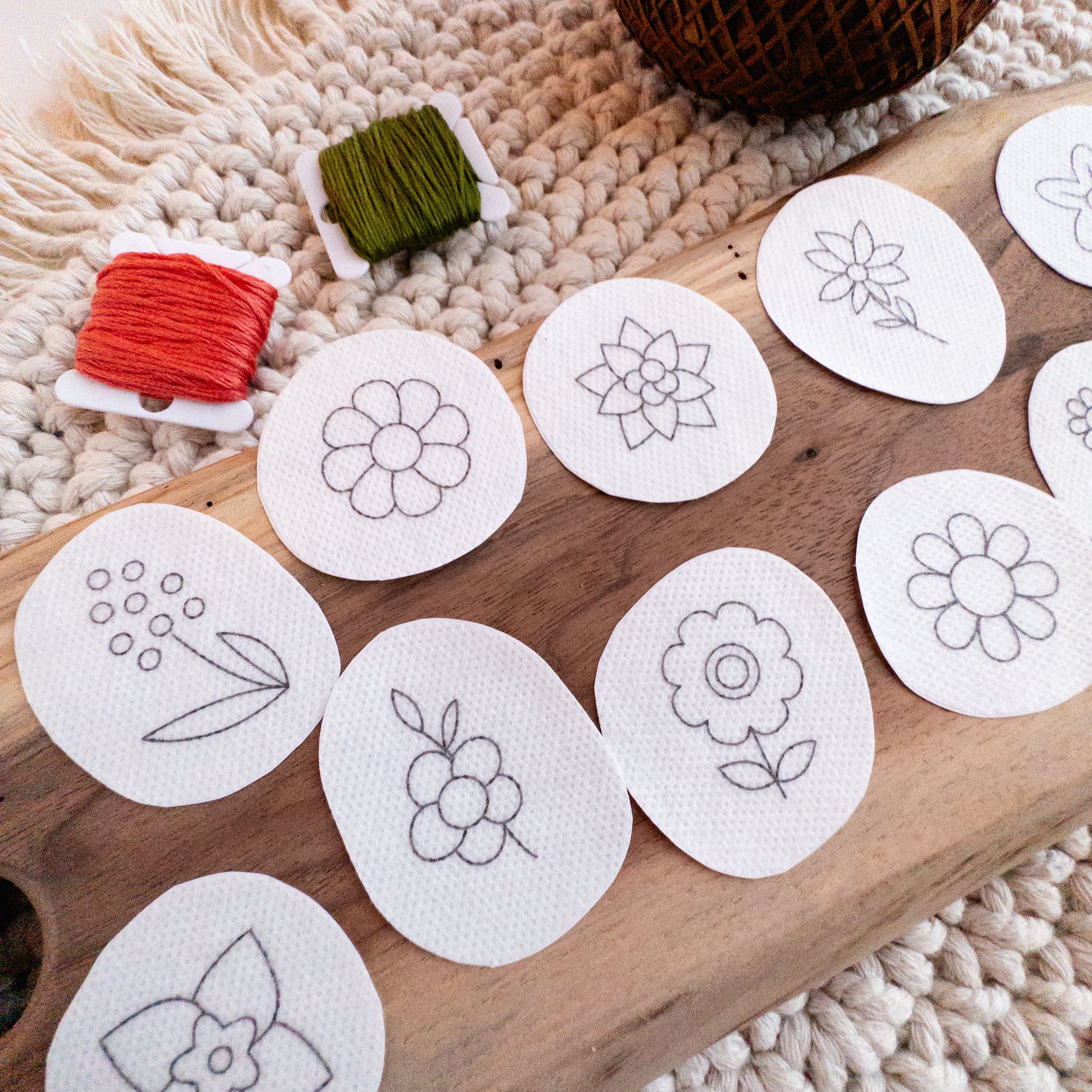 White oval stick and stitch mini flower embroidery patterns on a wooden board with red and green floss.