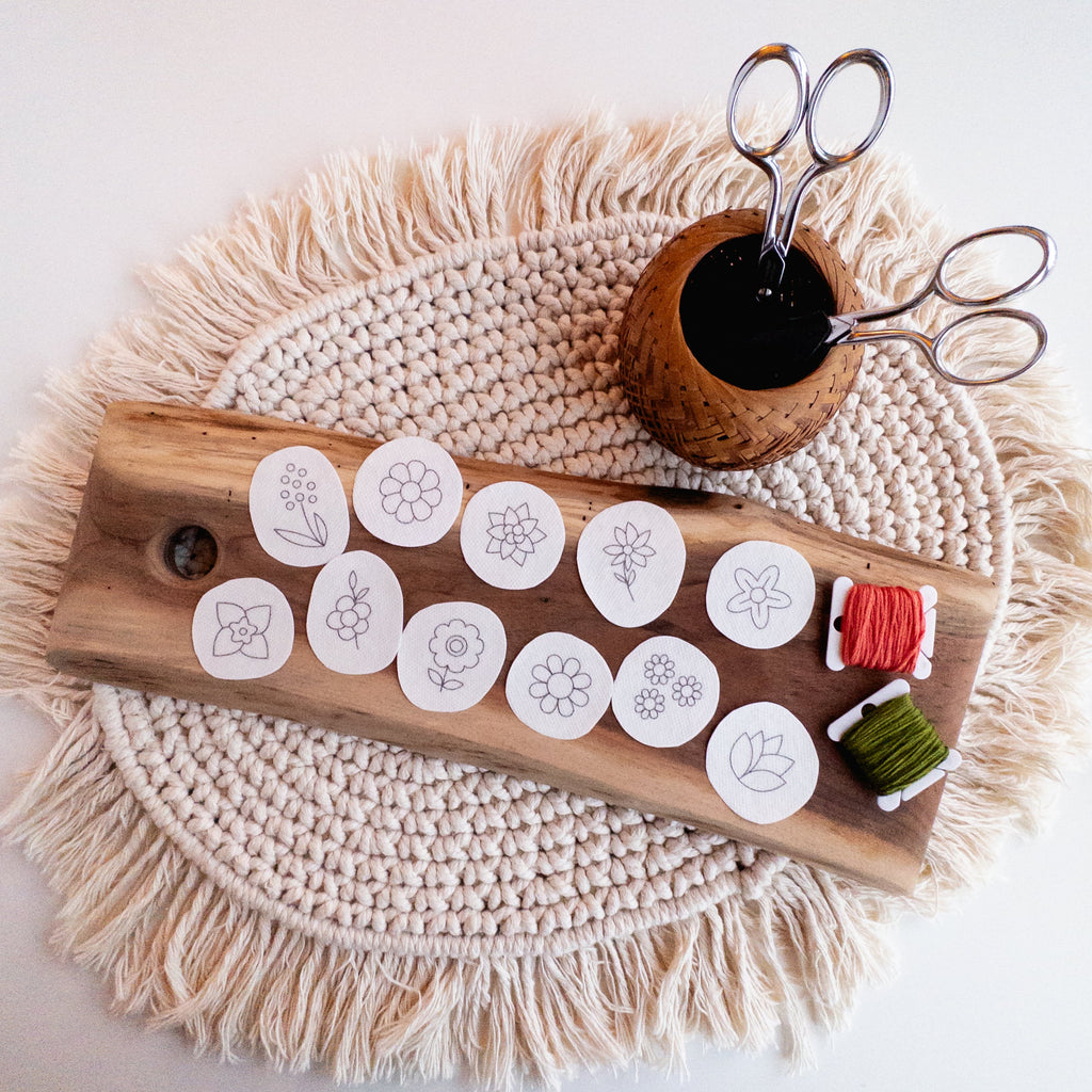 12 white round stick and stitch mini flower embroidery patterns on a wood board with thread and scissors.