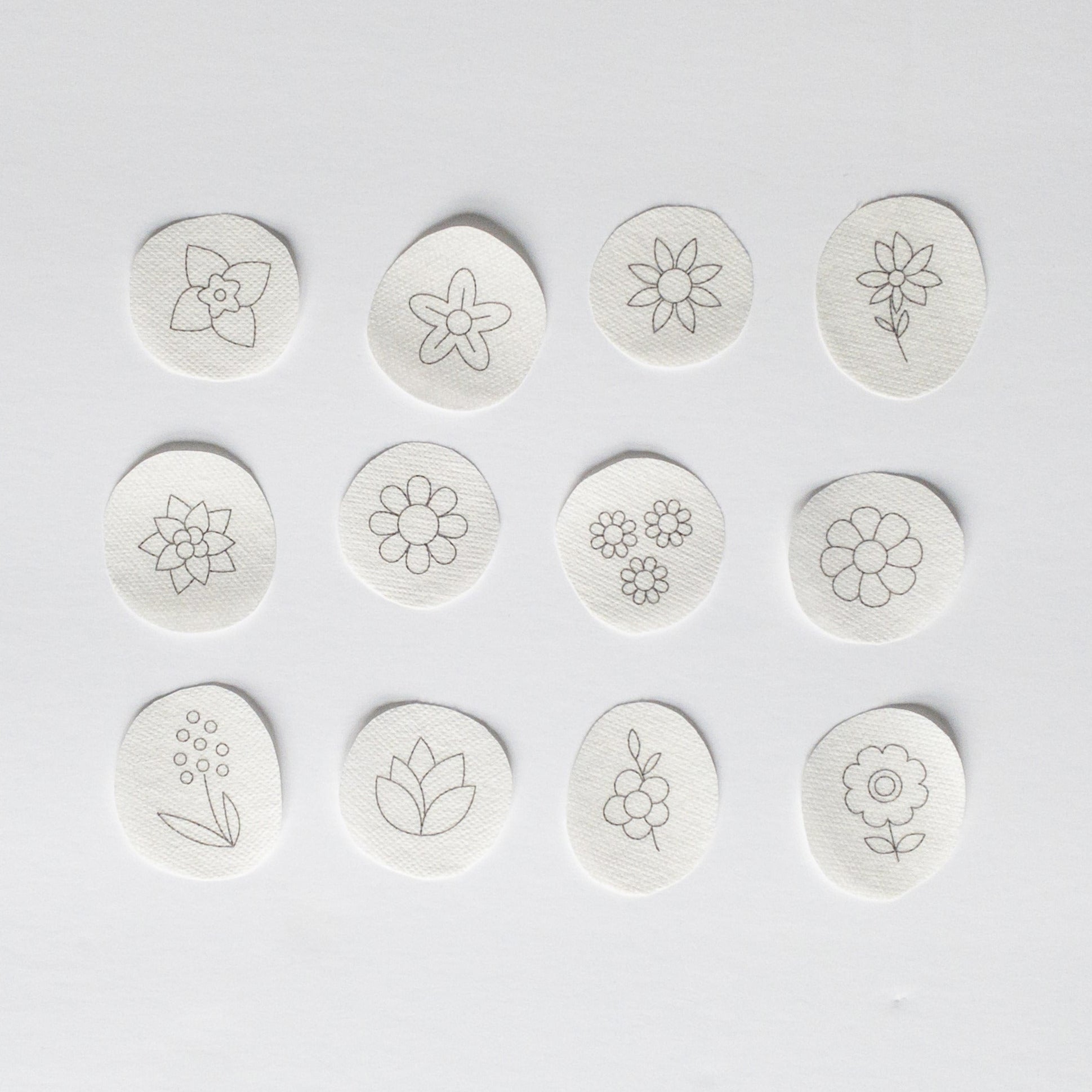 Twelve white water-soluble stick and stitch mini flower embroidery patterns with black outlines.
