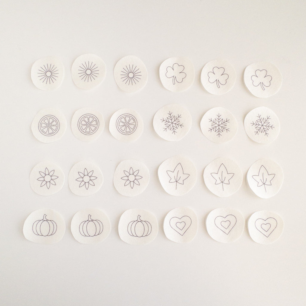 24 mini stick and stitch embroidery patterns on water-soluble stabilizer, featuring hearts, snowflakes, sunbursts, shamrocks, leaves, flowers, orange slices, and pumpkins.