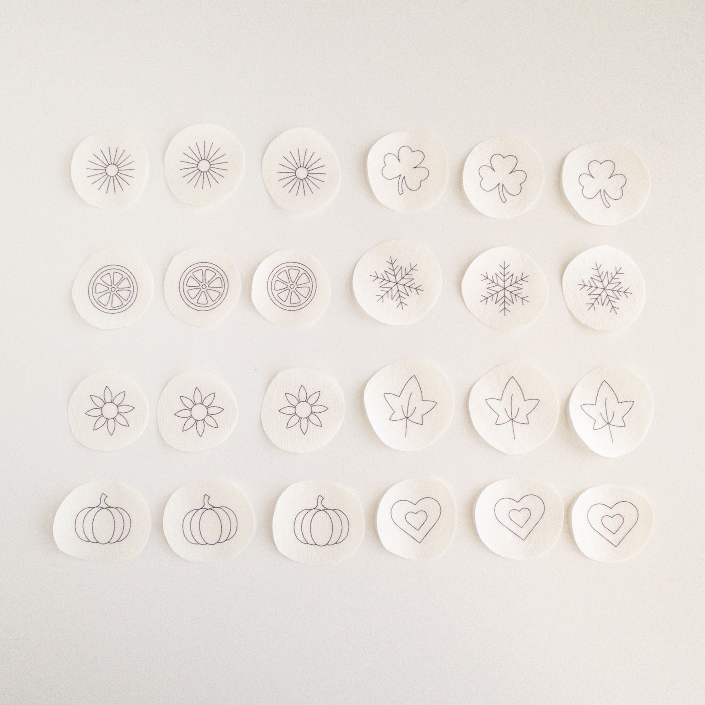 24 mini stick and stitch embroidery patterns on water-soluble stabilizer, featuring hearts, snowflakes, sunbursts, shamrocks, leaves, flowers, orange slices, and pumpkins.