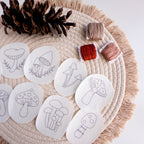 Nine mushroom stick and stitch embroidery patterns on white water-soluble stabilizer, with brown, red, and peach floss.