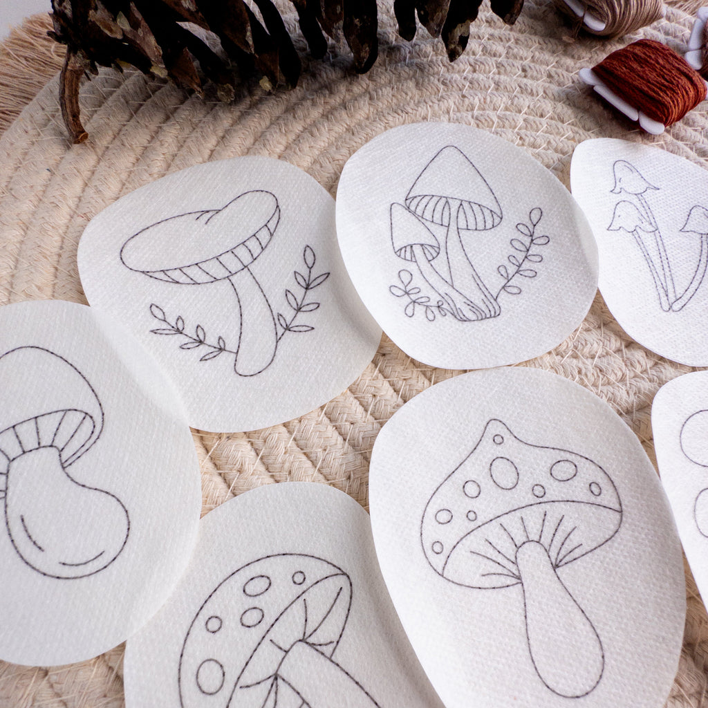 White water-soluble stabilizer patches with various black outline mushroom embroidery patterns on a woven mat.