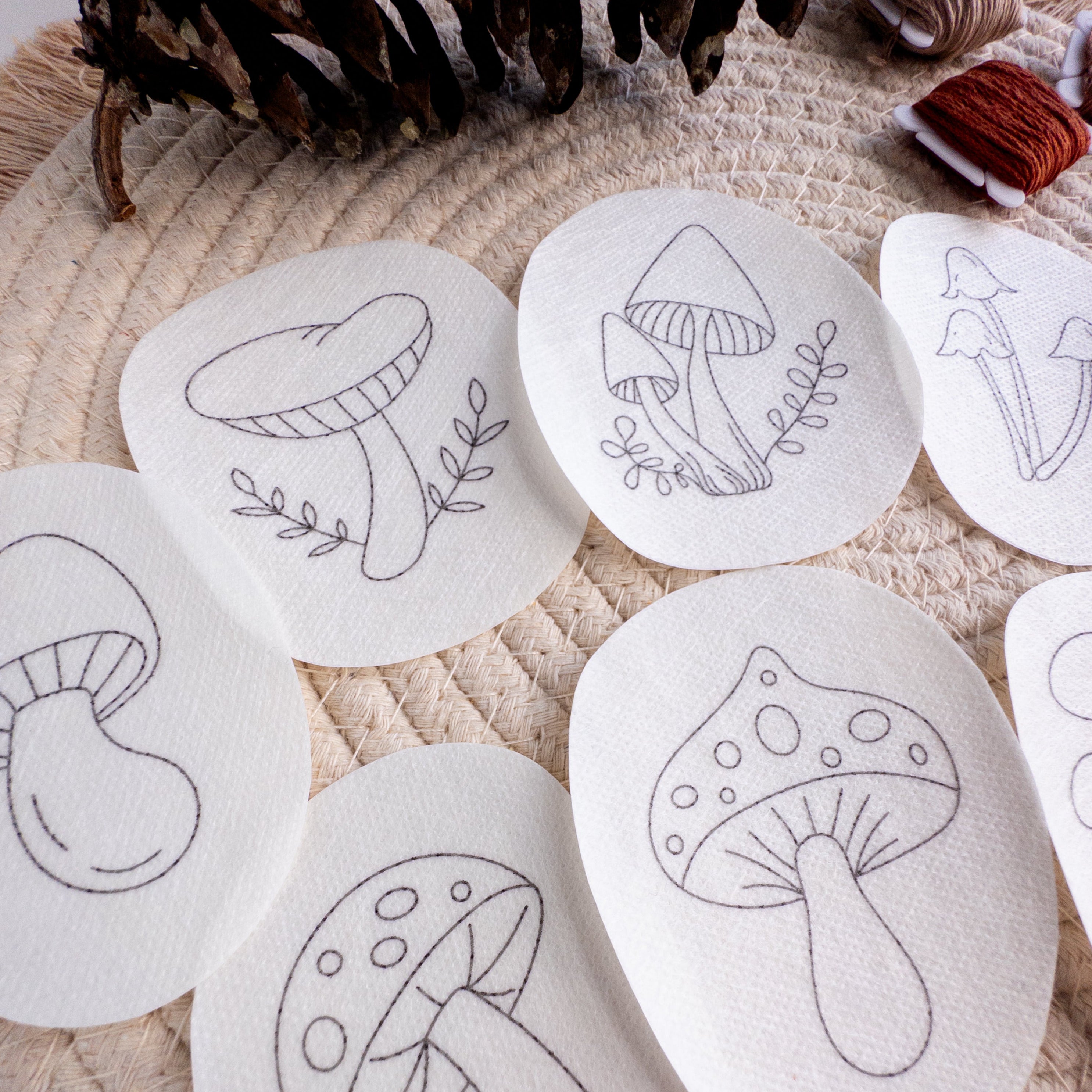 White water-soluble stabilizer patches with various black outline mushroom embroidery patterns on a woven mat.
