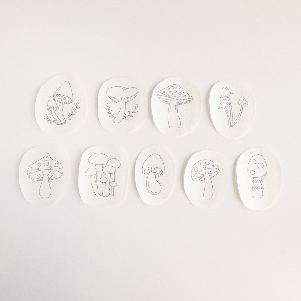 Nine oval, white water-soluble stabilizer patches with unique black line art mushroom embroidery patterns.