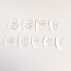 Nine oval, white water-soluble stabilizer patches with unique black line art mushroom embroidery patterns.